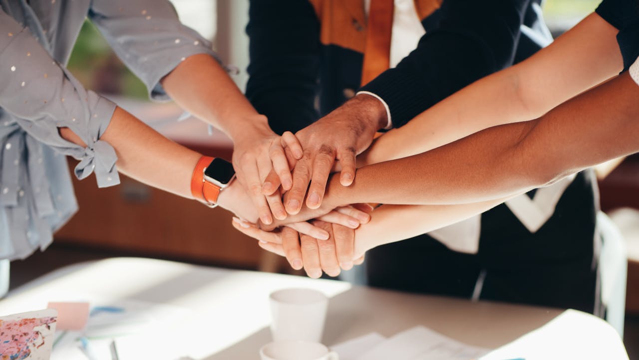 A close-up shot of diverse team members stacking hands over a white table, symbolizing unity and collaboration.